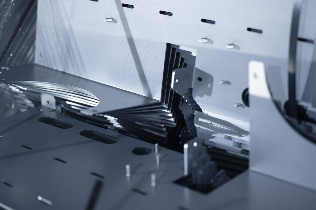 Close-up of blue-tinted industrial machinery with metal panels, screws and gear-like teeth in a precision device.