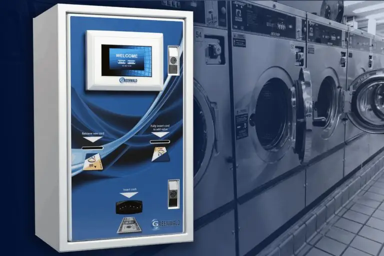 Blue self-service laundry payment kiosk with touchscreen in a laundromat, beside row of front-loading washers.