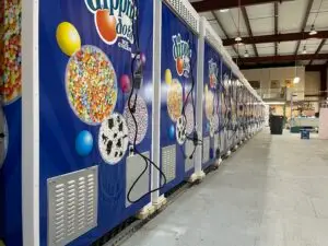 Row of blue Dippin' Dots ice cream vending machines in a warehouse, each displaying large candy-topped images with cords hanging from them